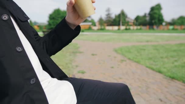 Hombre guapo camina en el parque y se sienta en un banco disfrutando de su sabroso café — Vídeos de Stock