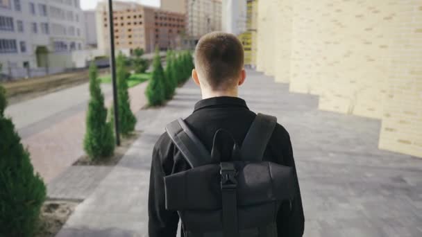 Jovem bonito homem de negócios pensativo caminha em uma área urbana moderna com uma mochila — Vídeo de Stock