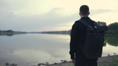 Sırt çantalı bir adamın, göl kenarında yürüdüğü yakın plan dikiz görüntüsü.
