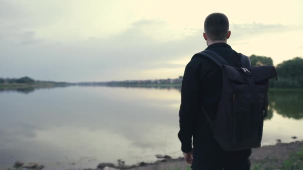 Vista trasera de cerca de un hombre con una mochila caminando cerca de un lago, paisaje — Vídeo de stock