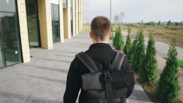 Joven turista con una mochila caminando cerca de un centro comercial en un día soleado — Vídeos de Stock