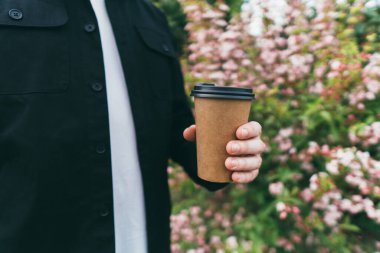 Parktaki güzel çiçeklerin arka planında bir adam kahve tutuyor.