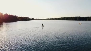 Gün batımında nehir dalgası boyunca sörf tahtasında yüzen bir sörfçünün hava görüntüsü.