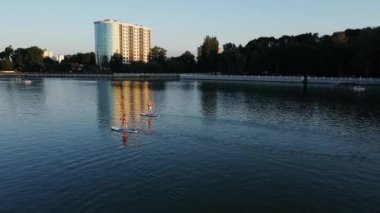 Göl manzaralı insanlar can yeleğiyle sörf tahtasında yüzmeyi öğrenirler.