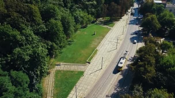 Stary tramwaj z ludźmi przechodzi w mieście w pobliżu parku w słoneczny dzień — Wideo stockowe