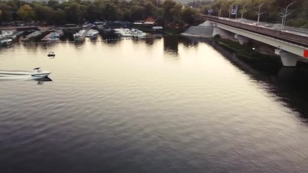 O barco navega sob uma ponte que corre o metrô ao pôr do sol em áreas urbanas. — Vídeo de Stock