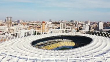 Olimpik futbol stadyumunun yanında büyük bir şehrin arka planına doğru uçuyor.