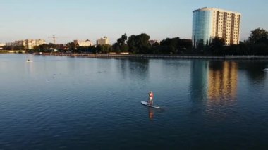 Göldeki bir adamın havadan görünüşü, can yeleğiyle sörf tahtasında yüzen bir çalışma.
