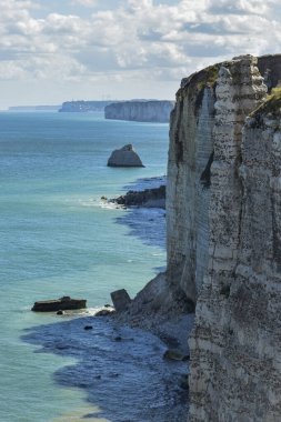 Normandiya 'da etretat ikonik uçurumlarının dikey yaz manzarası, canlı turkuaz deniz, desenli dalgalar ve yeşile bürünmüş yüksek beyaz kaya oluşumları - nefes kesen bir kıyı kaçışı..