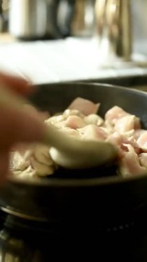 Dikey 4K videosu. Bir erkeğin eli kızartma tavasında kızartılmış eti ahşap bir spatulayla karıştırır. Modern yemek ve sağlıklı yemek teması.