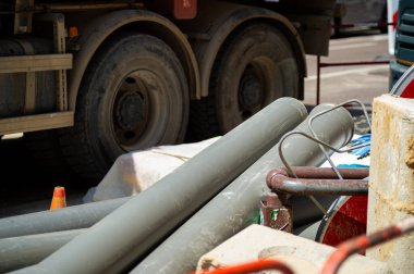 İnşaat alanında ağır bir kamyonun yakın çekimi. Altyapı boruları ve beton bloklar düzgünce istiflenmiş, kurulum için hazır. Turuncu bir trafik konisi de görülebilir.