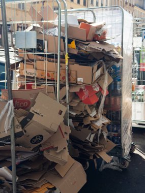Versailles, France - 18 September 2025: A large quantity of used cardboard packaging is piled high in metal roll cages outside a grocery store. This vertical image shows post-delivery waste.