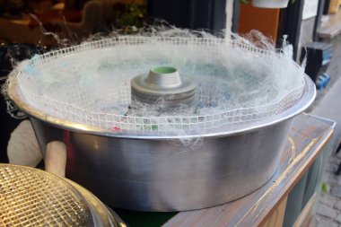 Vendor cotton candy machine with stainless bowl and airy sugar threads in motion. Great for concepts of dessert, street food, fair treats, cooking process, equipment and production.