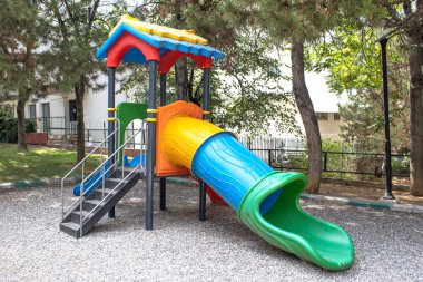Colorful plastic playground with tube slide, stairs and canopy in a public park. Useful for family brochure, childcare ad, urban recreation design, safety guide, education material, website banner.