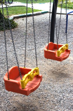 Two toddler swings hanging on chains in a green park playground. Perfect for parenting content, public space design, childhood wellness, safety education, brochure, banner, website header.