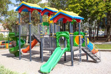 Wide view of outdoor playground with several slides, ladders and platforms surrounded by trees. Perfect for family magazine, childcare brochure, urban park promotion, safety and education use.