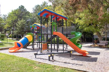 Bright plastic playset with tunnel slide, spiral slide and seesaw in a green park. Useful for education, recreation, childcare brochure, urban planning article, parenting blog or safety guide.