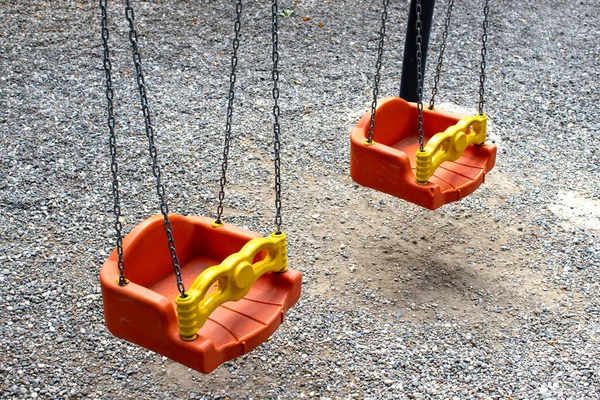 Two toddler swings hanging on chains in a green park playground. Perfect for parenting content, public space design, childhood wellness, safety education, brochure, banner, website header.