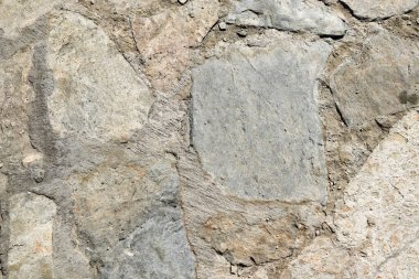 Close-up of rough natural stone masonry with cement joints. Neutral gray-beige surface for architecture visuals, backgrounds, patterns, mockups, materials and construction or renovation concepts.