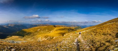 Romanya 'nın Parang Dağları' ndaki Galcescu Gölü yakınlarındaki vahşi Karpatlar 'da, canlı sonbahar renklerinin engebeli doruklarla buluştuğu nefes kesici bir sonbahar günü yaşayan bir gezgin görülüyor.