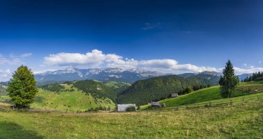 Romanya 'nın Brasov kenti yakınlarındaki Moeciu Köyü' nde huzurlu bir sonbahar manzarası. Karpat Dağları 'nın kırsal manzarası sıcak sonbahar renklerinde, yuvarlanan tepelerle, geleneksel ahşap evlerle boyanmıştır.