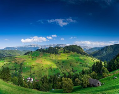 Romanya 'nın Brasov kenti yakınlarındaki Moeciu Köyü' nde huzurlu bir sonbahar manzarası. Karpat Dağları 'nın kırsal manzarası sıcak sonbahar renklerinde, yuvarlanan tepelerle, geleneksel ahşap evlerle boyanmıştır.