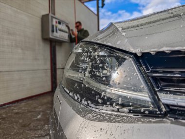 Araba yıkama, arabanın ön tarafı yakın plan, arka plandaki adam yıkama ücretini ödüyor.