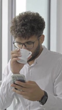 A young professional checks his smartphone while sipping coffee, showcasing modern work-life balance.