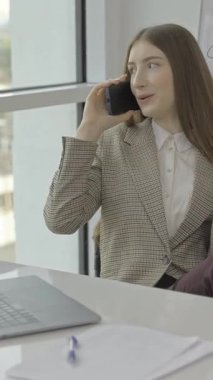 A young businesswoman converses on the phone in her stylish office, showcasing professionalism and communication.