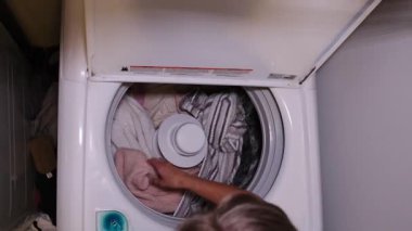 An individual is diligently loading a variety of different clothes into a washing machine for laundry purposes