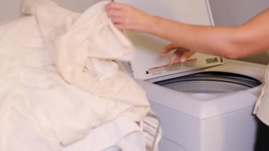 A person meticulously loads a washing machine with bedding and towels, highlighting routine laundry care practices
