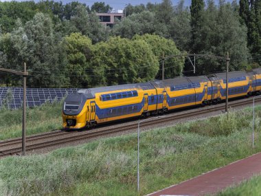 Dutch passenger train passing solar panel installation in green energy corridor