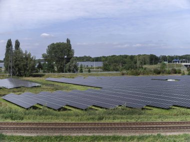 Large-scale solar panel installation adjacent to railway tracks with industrial background