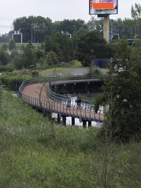 Curved pedestrian bridge with cyclists and urban infrastructure in background