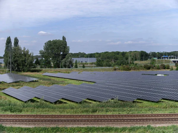 Large-scale solar panel installation adjacent to railway tracks with industrial background