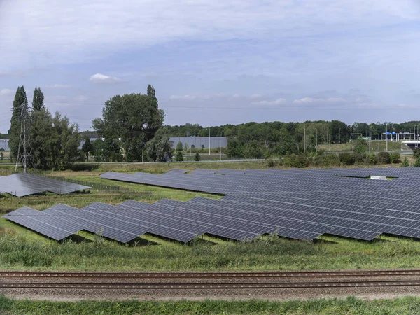 Large-scale solar panel installation adjacent to railway tracks with industrial background