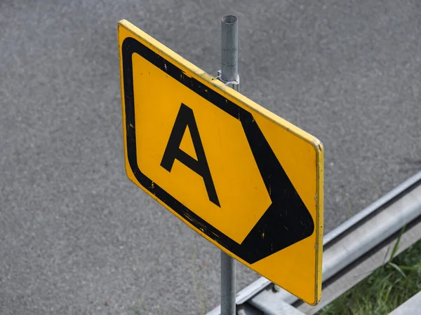 Yıpranmış sarı yol işaretinin ayrıntılı görüntüsü, montaj donanımlı A harfini gösteriyor.