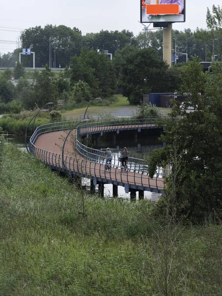Curved pedestrian bridge with cyclists and urban infrastructure in background