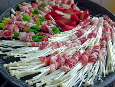 Akşam yemeği ya da parti için leziz yemek pişirmek için soğanlı et ruloları, taze soğan ve dilimlenmiş sosis bir ızgara tavasında hazırlanır..