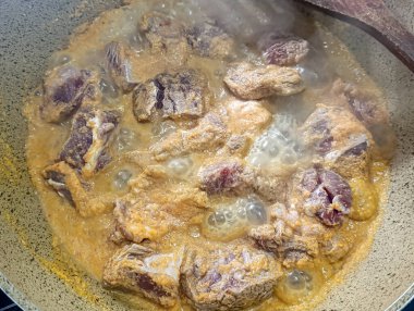 Et bir tavanın içinde et suyu kaynıyor, pişerken buhar çıkarıyor, görünür bir tahta kaşıkla, mutfak temalı içerik için idealdir..