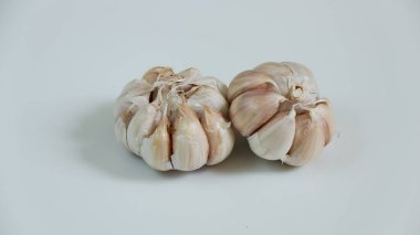 İki taze sarımsak soğanı beyaz bir yüzeye oturmuş karanfillerini sergiliyor. Yemek tarifleri ve yemek hazırlama içeriği için mükemmel..