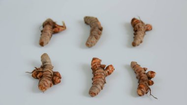 Taze zerdeçal kökleri beyaz bir yüzeye dizilir ve doğal formlarını ve renklerini gösterir. Yemek malzemelerini ve sağlık kavramlarını resmetmek için uygundur..