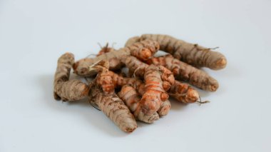 Birkaç ham zerdeçal kökü, yemek pişirme ve sağIık uygulamalarında kullanılmayı bekleyen düz beyaz bir yüzey üzerinde bir araya toplanmıştır..