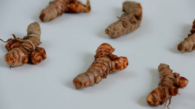 Taze zerdeçal kökleri temiz beyaz bir yüzeye dağılır, doğal dokularını ve renklerini vurgulayarak sağlıklı yemek ve pişirme projeleri için ideal hale getirirler..