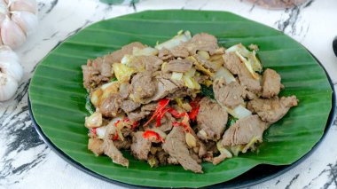 Canlı yeşil muz yaprağı tabağında taze sebzelerle karıştırılmış tuzlu et sunuluyor. Bu da onu mutfakla ilgili içerik için ideal kılıyor..