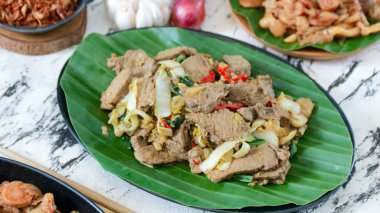 Lezzetli kızarmış et ve sebze yemeği canlı yeşil muz yaprağı üzerinde sunuluyor. Restoran menüleri ve yemek fotoğrafçılığı için mükemmel servis edilmeye hazır..