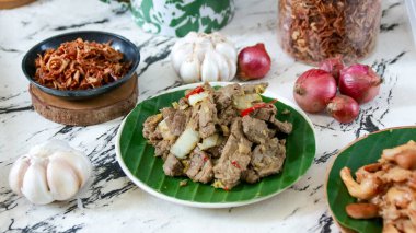 Yakın plan biftek kızartması, sarımsak, soğan ve baharatla, muz yaprağı tabaklarında hazırlanır, taze ve lezzetli bir yemek yaratır, yemek blogları için mükemmeldir..