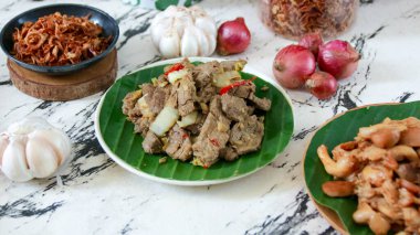 Lezzetli kızartılmış biftek, yeşil yaprakların üzerinde soğan ve sarımsakla servis edilir ve mermer bir yüzeye yerleştirilir. Asya mutfağını sergilemek için idealdir..