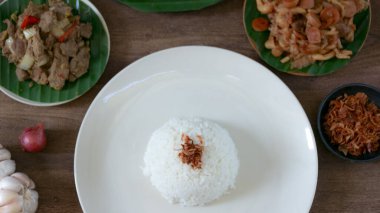 Çeşitli garnitürlerle servis edilen pirinç ahşap bir masada sunulur, basit ve iştah açıcı bir yiyecek düzeneği oluşturur. Mutfak ve yaşam tarzı için mükemmel..
