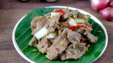 Canlı bir muz yaprağı tabağında soğan ve kırmızı biberle servis edilen tuzlu sığır kızartması iştah açıcı ve taze bir görünüm yaratıyor. Mutfak ve sağlıklı yemek içeriği için mükemmel..